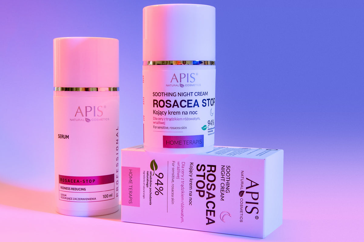 Three skincare products from the brand APIS are arranged on a pink-to-purple gradient studio background. The set includes a Rosacea-Stop serum, a Soothing Night Cream bottle, and a Rosacea-Stop box.
