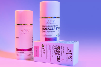 Three skincare products from the brand APIS are arranged on a pink-to-purple gradient studio background. The set includes a Rosacea-Stop serum, a Soothing Night Cream bottle, and a Rosacea-Stop box.