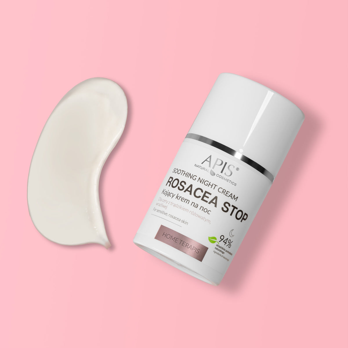 A white cylindrical cosmetic bottle labeled APIS Soothing Night Cream Rosacea Stop, shown on a soft pink background with a curved smear of white cream beside it.